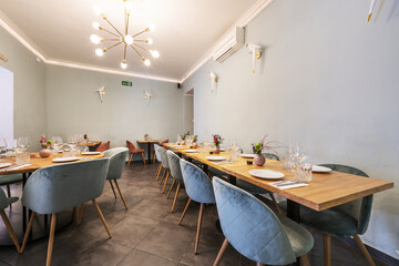 Long light wood dining table with green velvet upholstered stools in a bar dining room with multi-bulb lamps, light green walls and gray tiled floors