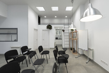 An empty classroom with high ceilings, pendant lamps and lots of black armrest chairs with a swivel table, a white board for erasable ink markers