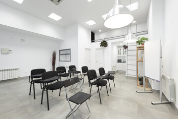 Fototapeta premium An empty classroom with a bunch of black chairs with armrests with a swing table, a whiteboard for deleble ink markers