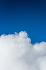 Some fluffy clouds high up and a plane in the distance
