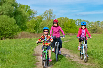 Happy mother and kids on bikes cycling outdoors in park, active family sport  and fitness together

