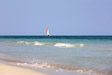 View to sailboat in blue ocean from sand beach and water surface. Background for sea holidays