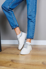Close-up of female legs in jeans and casual white sneakers. Women's comfortable casual shoes. White leather women's sneakers