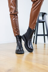 Slim female legs in black leather chelsea boots. Women's spring-autumn boots. Female legs in leather brown pants
