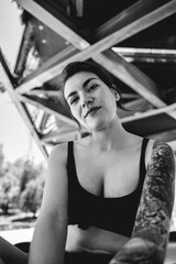 Rebel style: portrait of happy and sexy young woman with black top and short, tattoos and skateboard in urban skate park under a bridge (in black and white)