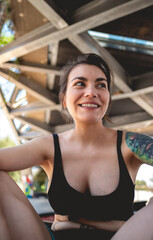 Rebel style: portrait of happy and sexy young woman with black top and short, tattoos and skateboard in urban skate park under a bridge