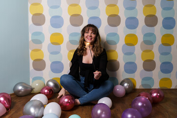 Young Woman Sitting Around Balloons with a Sparkler Against Colorful Background