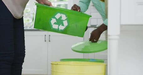 Senior diverse couple wearing shirts and segregating waste in kitchen