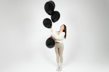 Young brunette in light clothes holding bunch of black balloons, isolated on white background.