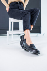 Fototapeta na wymiar Close-up of female legs in pants and black leather classic chelsea shoes. Women's comfortable summer shoes. New spring-summer collection of women's leather shoes 2023