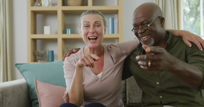 Portrait of happy senior diverse couple wearing shirts and making video call in living room