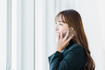 スマホで通話する笑顔のビジネスウーマン　日本人女性