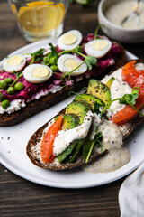 Two smorrebrods (open sandwiches with different toppings: avocado-salmon-cream cheese and quail eggs -beetroot - cream cheese) and glass of lemonade  on wooden table.