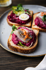 Three smorrebrods (open sandwiches) with toppings: herring, beetroot paste, quail eggs, avocado and mustard sauce on wooden table.