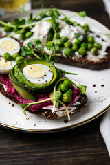 Two smorrebrods (open sandwiches) with different toppings: green peas - cottage cheese and quail eggs -beetroot paste- avokado- cream cheese on rye bread. 