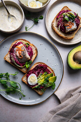Three smorrebrods (open sandwiches) with toppings: herring, beetroot paste, quail eggs, avocado and mustard sauce.