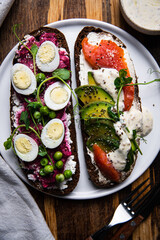 Two smorrebrods (open sandwiches with different toppings: avocado-salmon-cream cheese and quail eggs -beetroot - cream cheese) and mustard sauce on wooden board