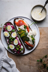 Two smorrebrods (open sandwiches with different toppings: avocado-salmon-cream cheese and quail eggs -beetroot - cream cheese) and mustard sauce on wooden board