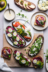 Mix of homemade smorrebrods (open sandwiches) with different toppings: avocado-salmon-cream cheese, herring-beetroot paste, green peas-cottage cheese, quail eggs -beetroot-cream cheese.