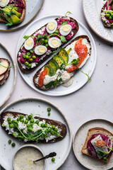 Mix of homemade smorrebrods (open sandwiches) with different toppings: avocado-salmon-cream cheese, herring-beetroot paste, green peas-cottage cheese, quail eggs -beetroot-cream cheese.