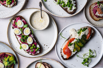 Mix of homemade smorrebrods (open sandwiches) with different toppings: avocado-salmon-cream cheese, herring-beetroot paste, green peas-cottage cheese, quail eggs -beetroot-cream cheese.