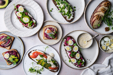 Mix of homemade smorrebrods (open sandwiches) with different toppings: avocado-salmon-cream cheese, herring-beetroot paste, green peas-cottage cheese, quail eggs -beetroot-cream cheese.