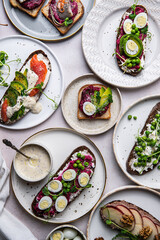 Mix of homemade smorrebrods (open sandwiches) with different toppings: avocado-salmon-cream cheese, herring-beetroot paste, green peas-cottage cheese, quail eggs -beetroot-cream cheese.