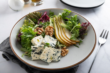 Healthy Salad made from Green Salad Leaves, Rocket Salad, Slices of Fresh Pears, pieces of Blue Cheese, Walnuts and Sesame Seeds.