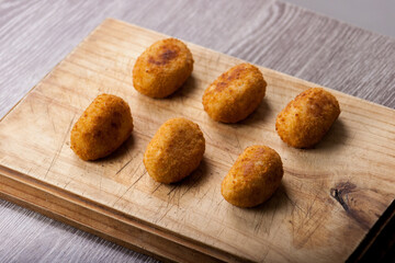 Classic Spanish croquettes on wooden board with dim light in the background. Fried potato.
