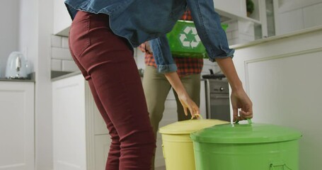 Diverse couple wearing shirt and jacket segregating waste in kitchen