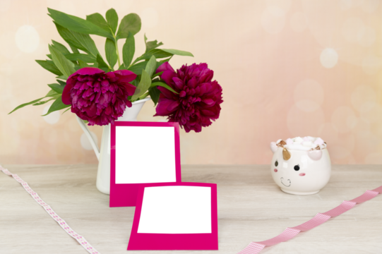 Mock up for square areas in pink frame. Peonies (Paeonia) in a white tin vase. A unicorn cup with marshmallows. Bright background in peach and pink tones with bokeh. Wood background and copy space.
