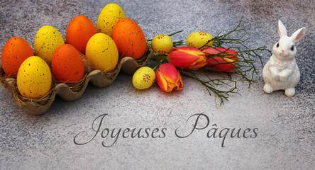 Carte de Pâques : lapin de Pâques assis devant des oeufs de Pâques jaunes et oranges avec le...