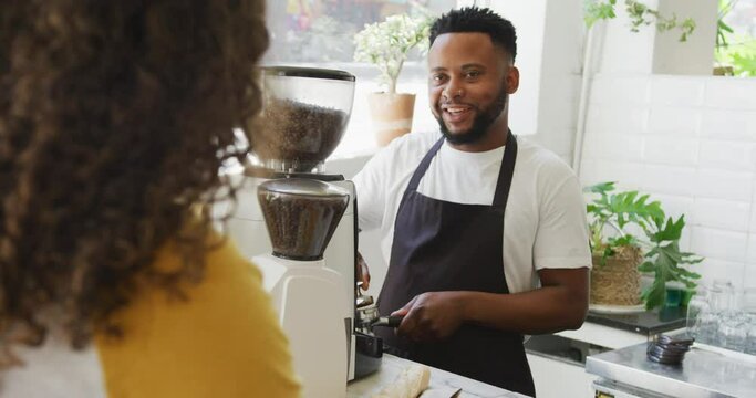 Happy african american male barista making coffee for biracial female client at cafe