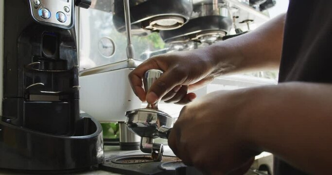 Close up of african american male barista making coffee using coffe machine at cafe