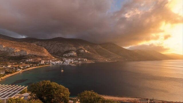 Panorama showing orange clouds during sunset on Amorgos island aerial timelapse from above. Traditional Greece - white houses on hills and turquoise sea, Cyclades