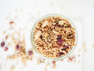Top view of glass jar filled with fresh granola with nuts and dried fruits placed on white table