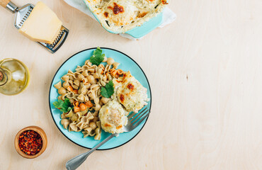 Baked cheesy meatballs casserole in the oven dish. Blue plate with with tomato and spinach pasta and meatballs
