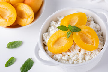 Fresh cottage cheese in white bowl with mint leaves and apricot pieces on white background