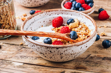 Healthy brakfast with yogurt and baked granola with berries in two small bowls, Granola baked with nuts, coconut oil and honey.