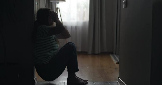 Silhouette of a sad woman sliding down the wall of her apartment