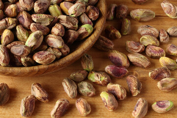 Peeled salted pistachios in a wooden bowl on a wooden table.