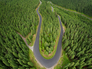 Aerial drone panorama above the wild coniferous forests of Sureanu Mountains. Transalpina asphalt highway winds through the woods. Summertime, Carpathia, Romania.