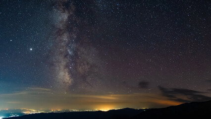 Milky way seen seen from the mountains, rising above urban city polution in a summer night. Astrophotography with stars and constellations.
