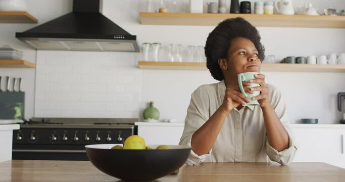 Happy african american woman drinking coffee in kitchen