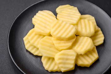 Raw fresh potatoes cut into slices on a black ceramic plate