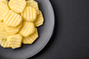 Raw fresh potatoes cut into slices on a black ceramic plate