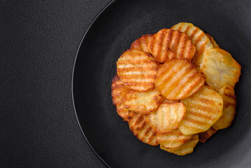 Delicious crispy fried potatoes in slices on a black ceramic plate