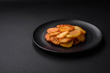 Delicious crispy fried potatoes in slices on a black ceramic plate