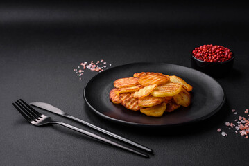 Delicious crispy fried potatoes in slices on a black ceramic plate