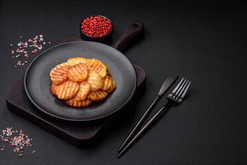 Delicious crispy fried potatoes in slices on a black ceramic plate